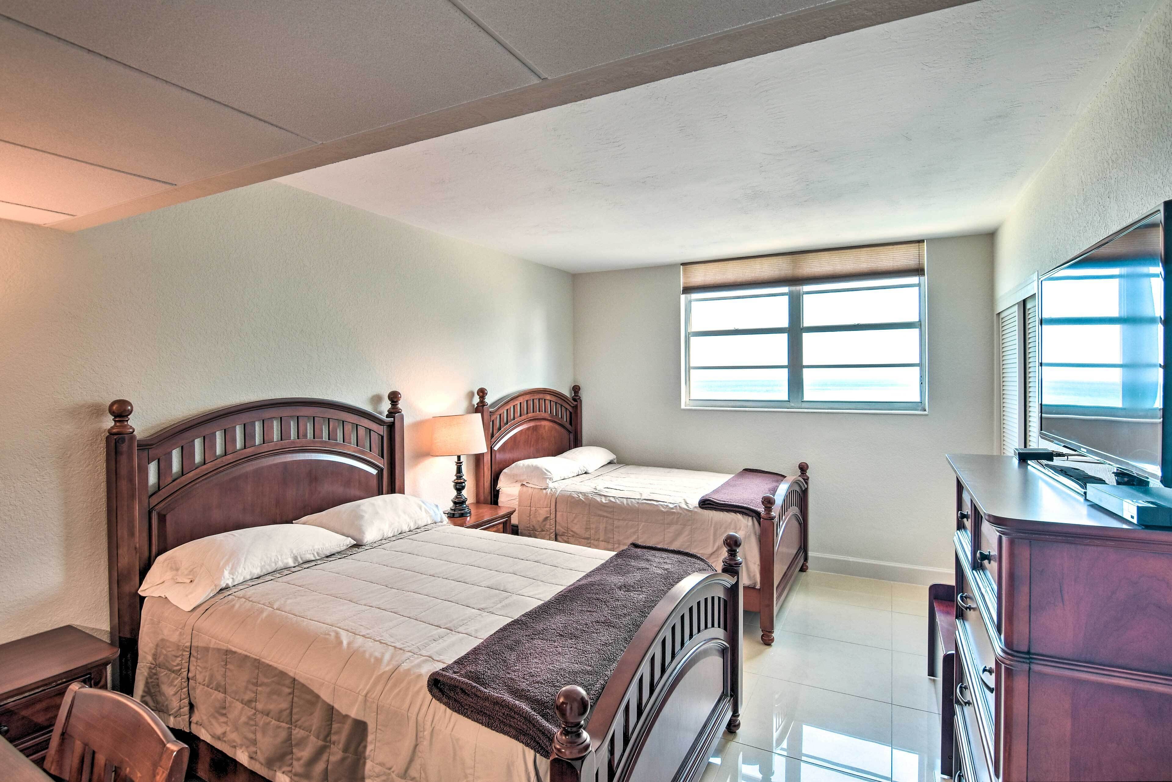 A hotel room with two wooden beds, a dresser, a desk, and a large window providing natural light.