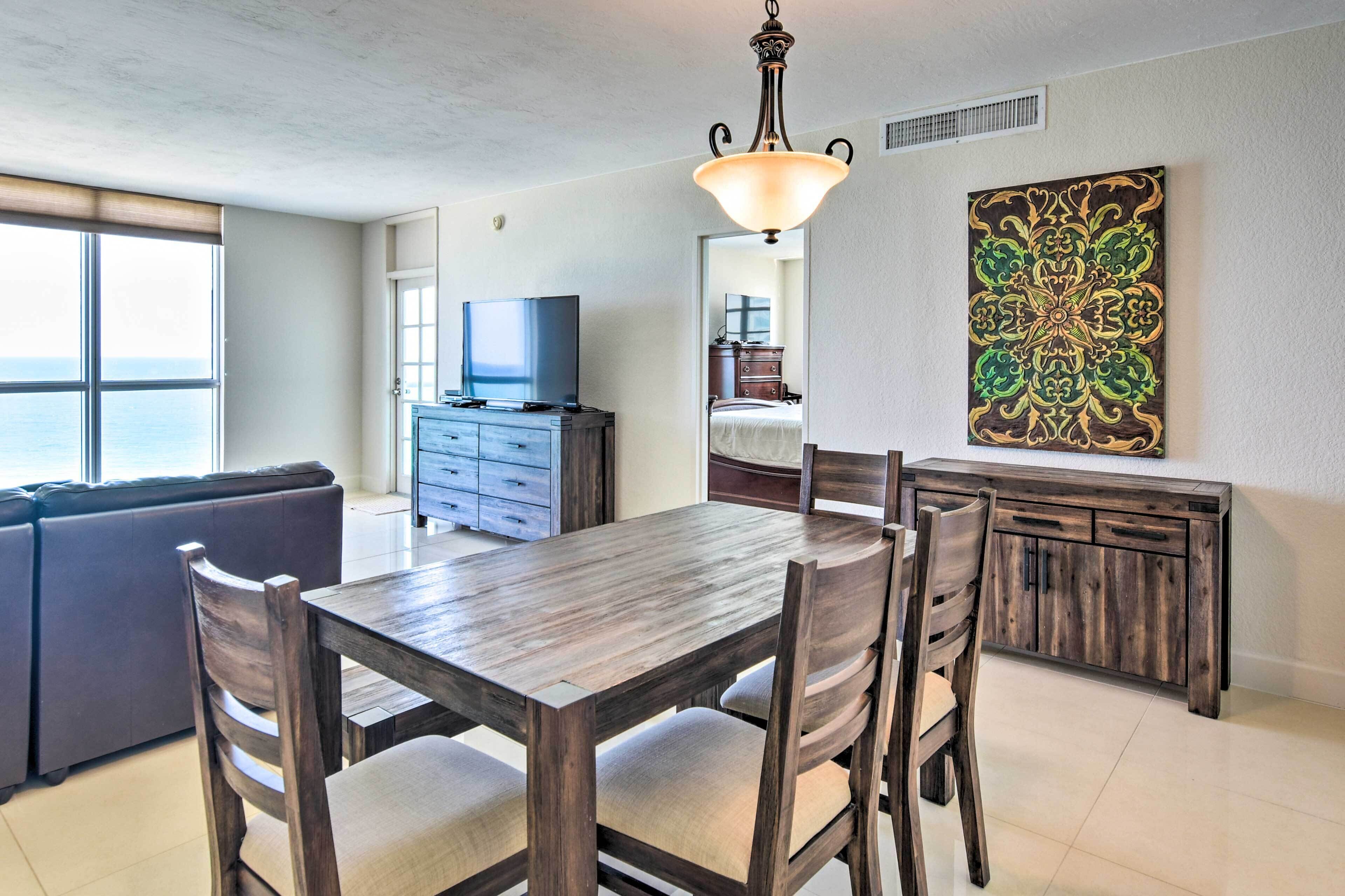 A dining area with a wooden table and chairs, a television, and a large decorative painting on the wall.