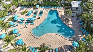 Vue aérienne d’un complexe hôtelier doté d’une grande piscine, de transats et de palmiers.