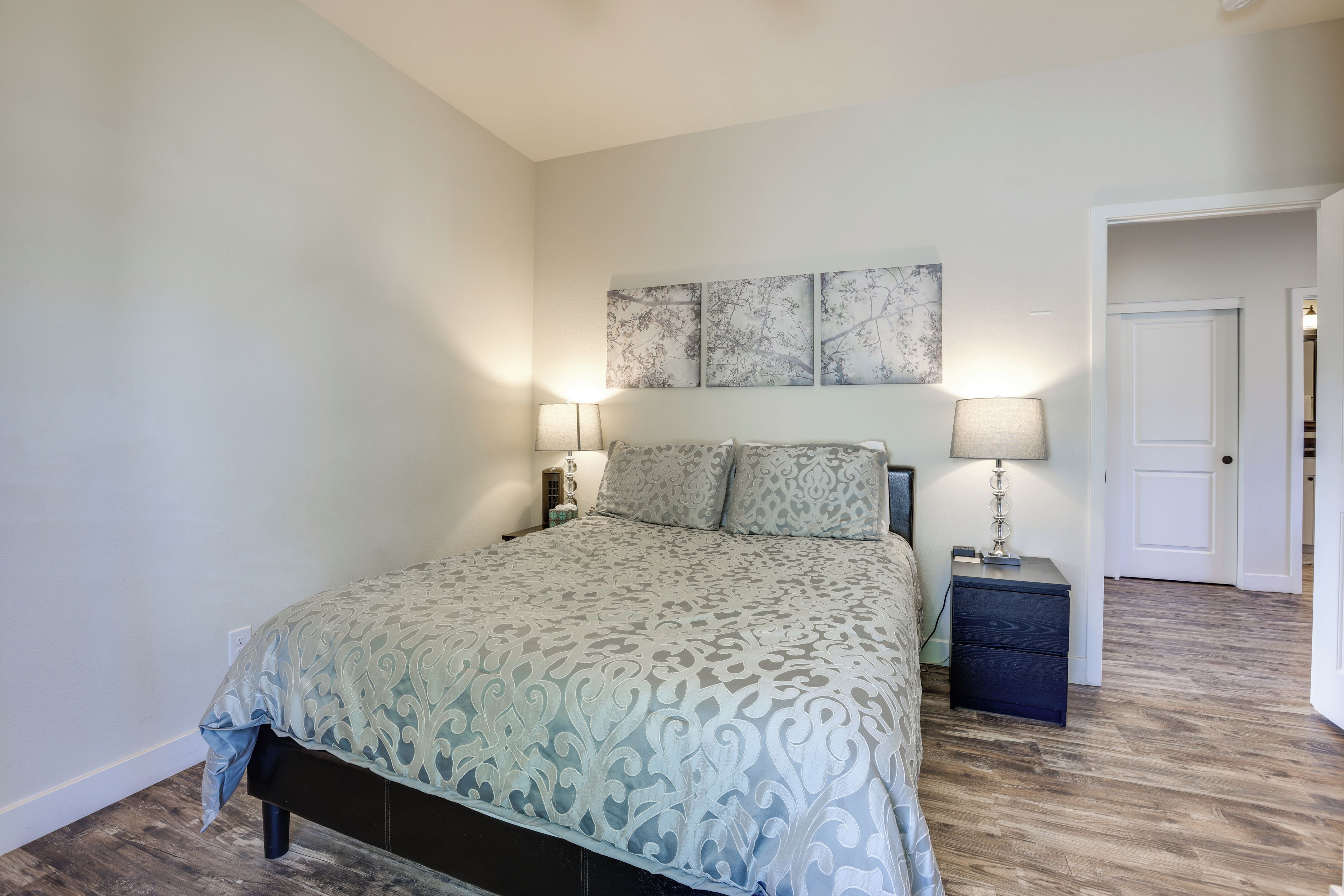 A bedroom with a bed, two bedside tables with lamps, a door, and a wall with three framed artworks.