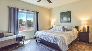 Une chambre à coucher avec un lit, des lampes de chevet, un ventilateur de plafond, une fenêtre avec des rideaux et un tableau au mur.