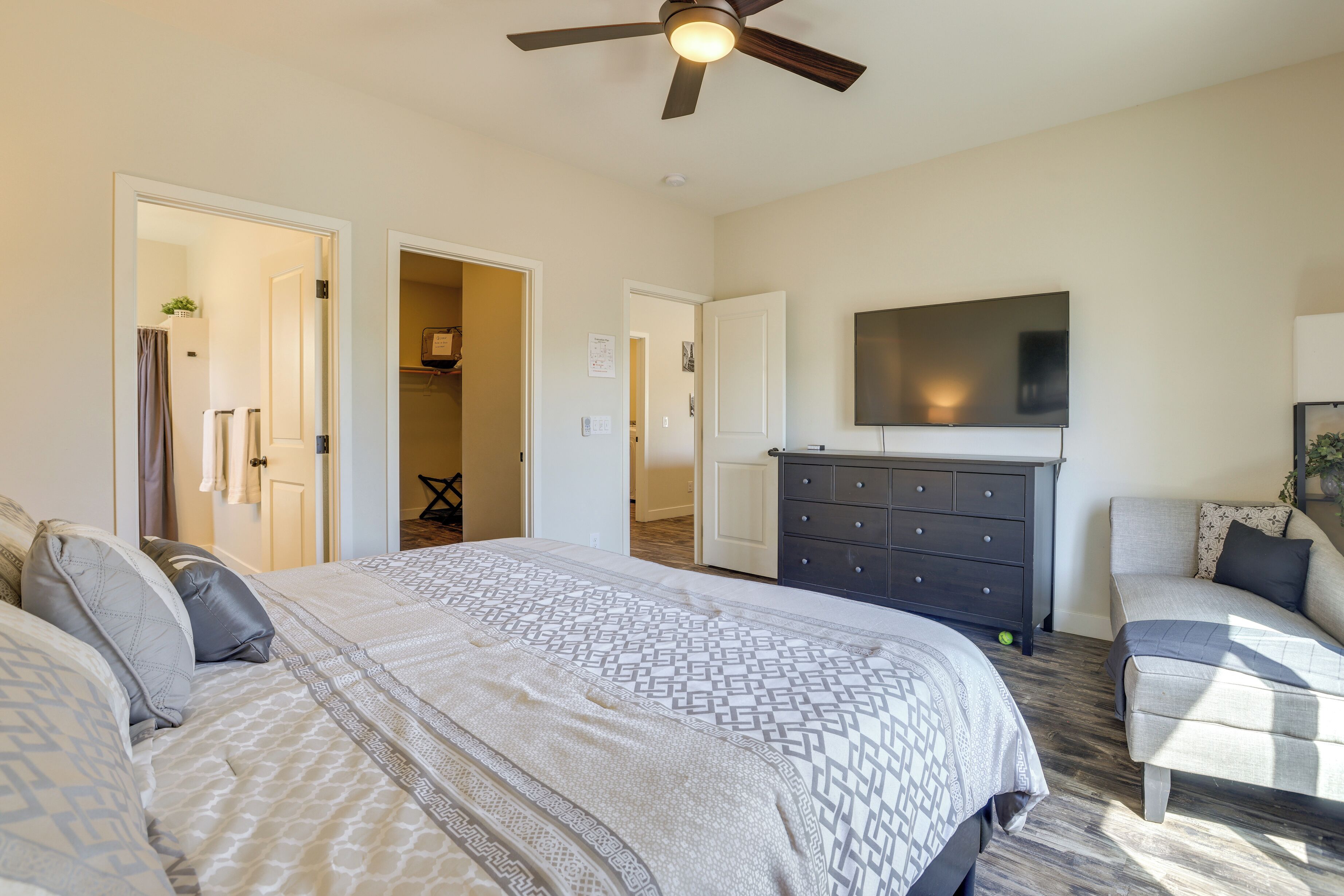 A bedroom with a large bed, a dresser, a TV on the wall, and a ceiling fan.