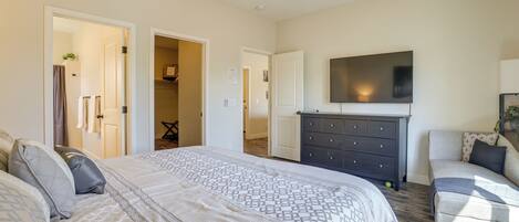 A bedroom with a large bed, a dresser, a TV on the wall, and a ceiling fan.