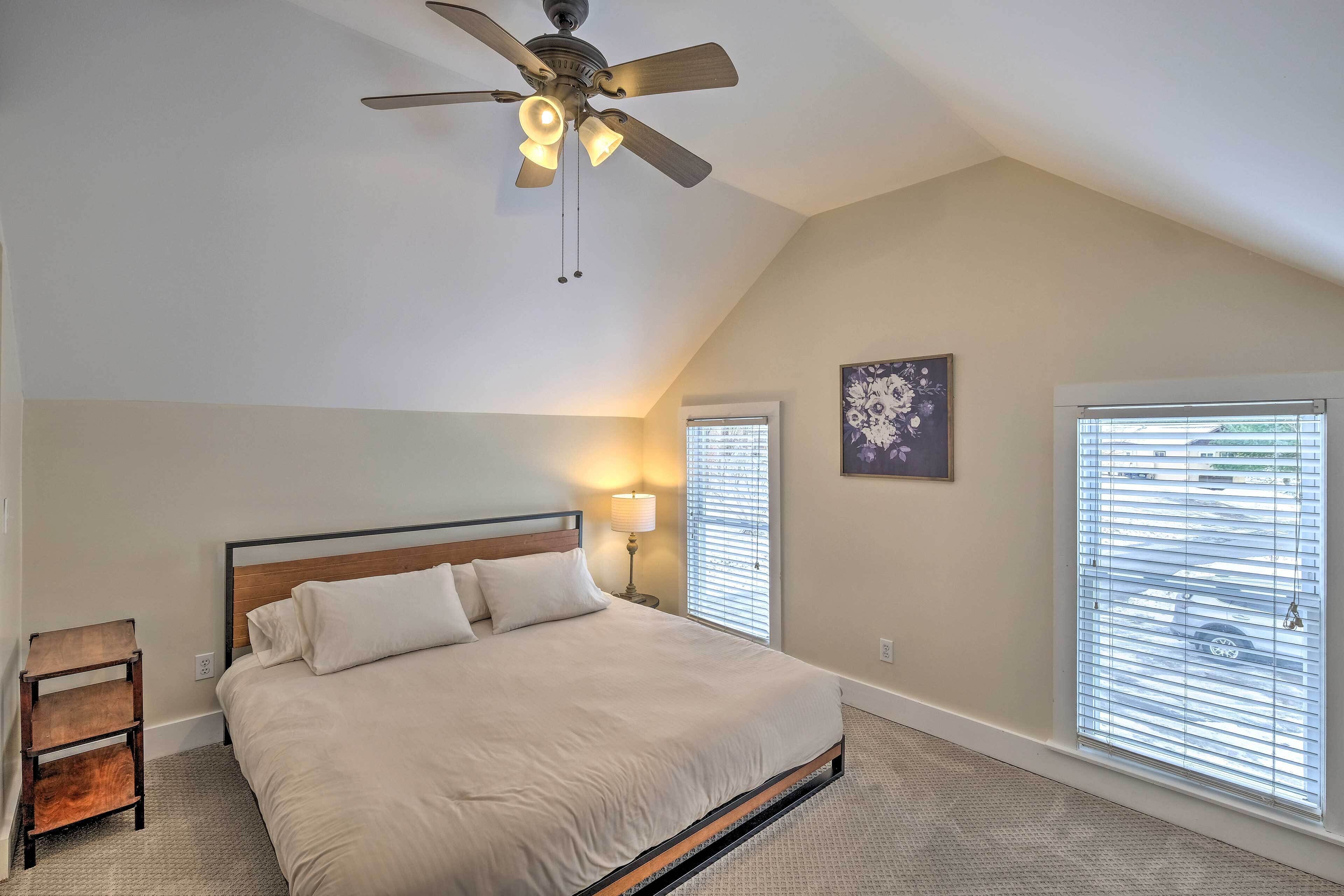 A bedroom with a bed, a nightstand, a ceiling fan, and two windows with blinds.