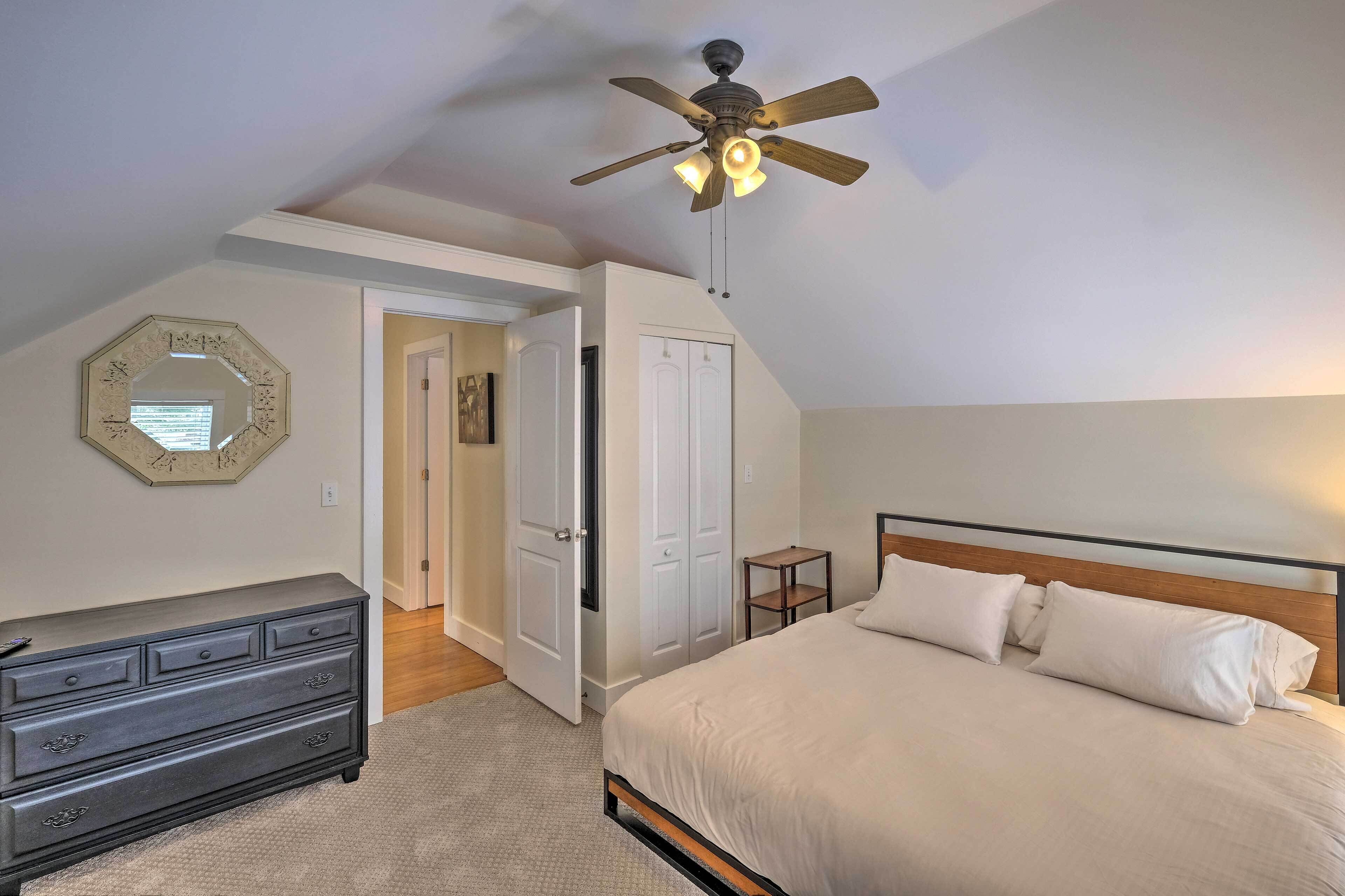 A bedroom with a bed, a dresser, a ceiling fan, and a door leading to another room.