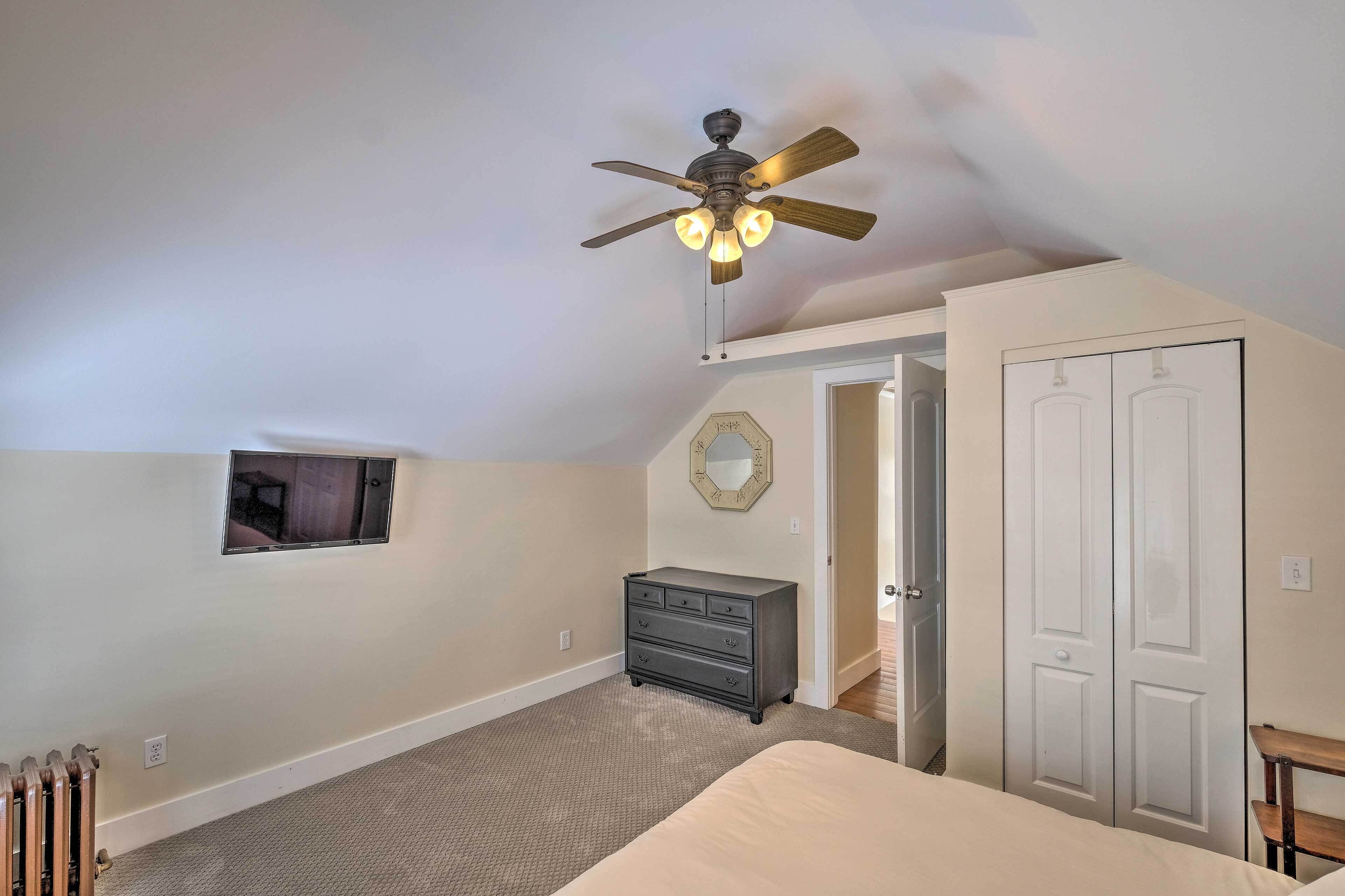 A bedroom with a ceiling fan, a dresser, a bed, and a door leading to another room.