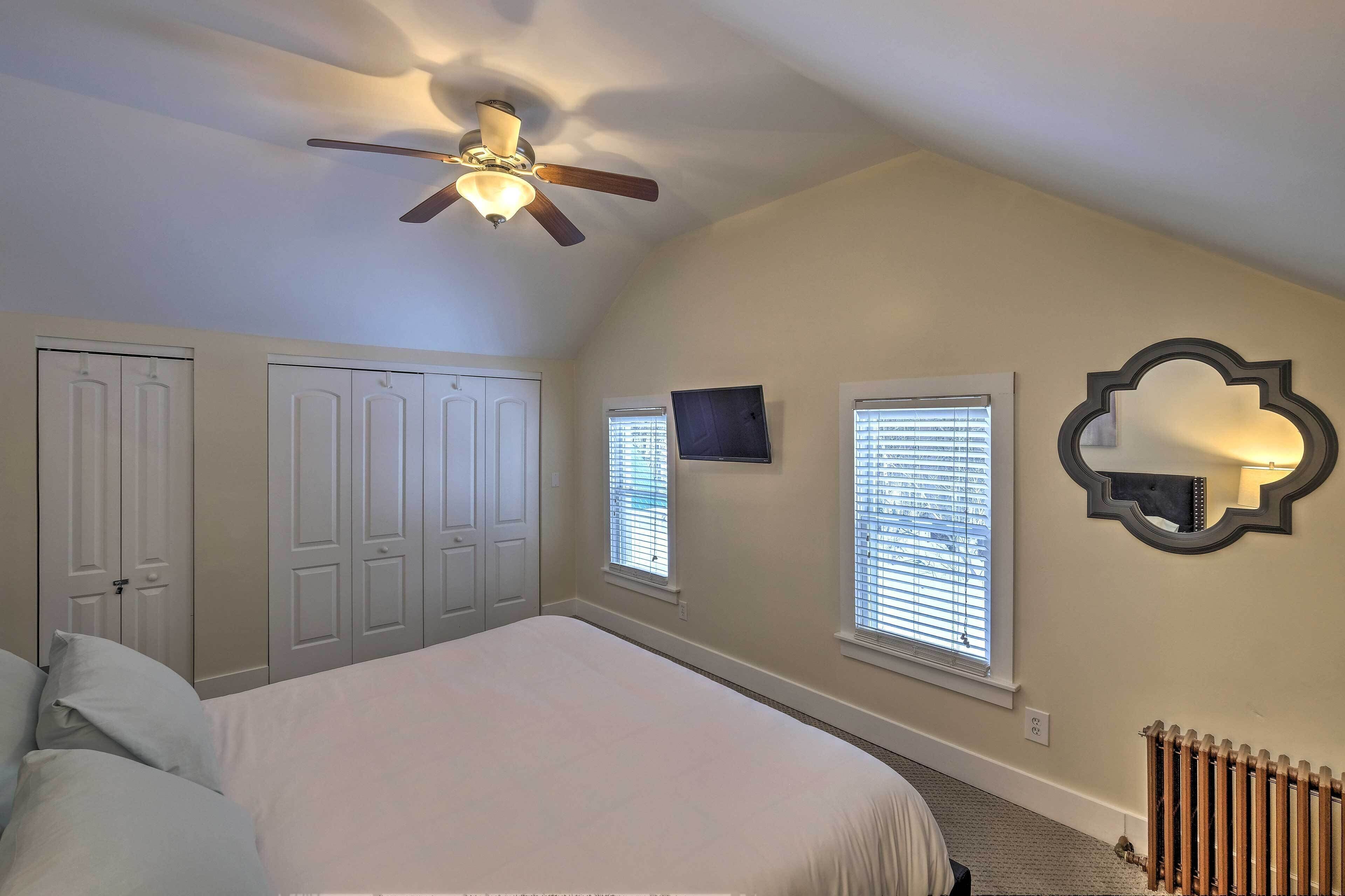 A bedroom with a bed, ceiling fan, wardrobe, TV, windows, and a radiator.