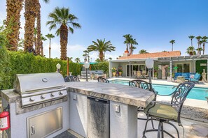 An outdoor kitchen with a grill, a pool, and a patio area with chairs and a sofa.