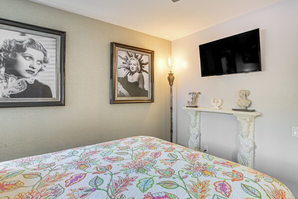 A bedroom with a bed, a television mounted on the wall, and a fireplace with decorative items.