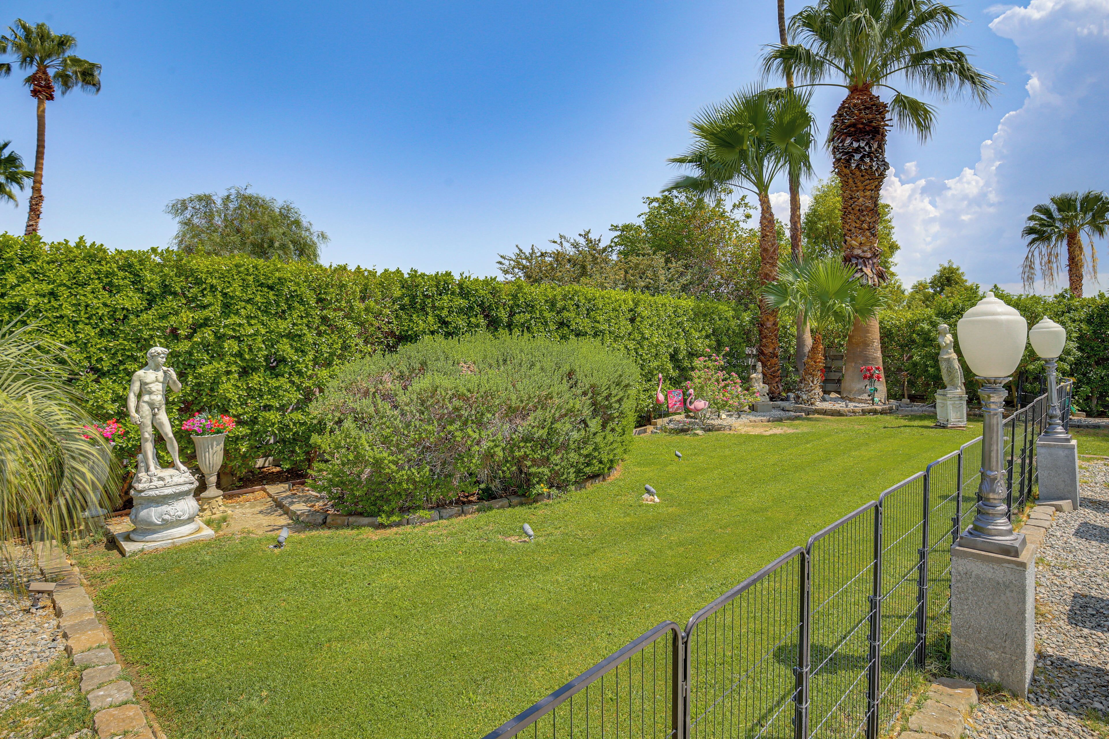 A well-maintained garden with a statue, palm trees, and a hedge.