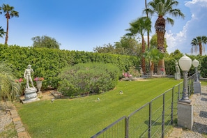 A well-maintained garden with a statue, palm trees, and a hedge.
