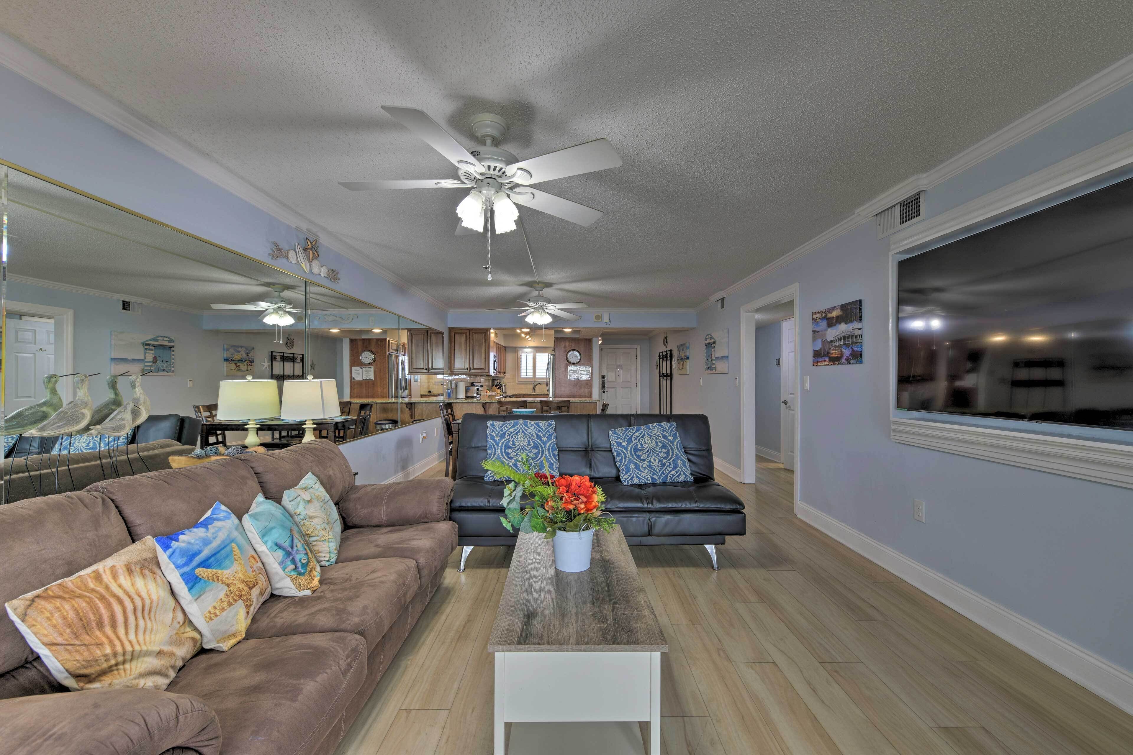 A spacious living room with a brown sofa, a coffee table with a vase of flowers, and a ceiling fan.