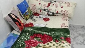 Een bed met een bloemenprint deken en kussens met geborduurde tekst.