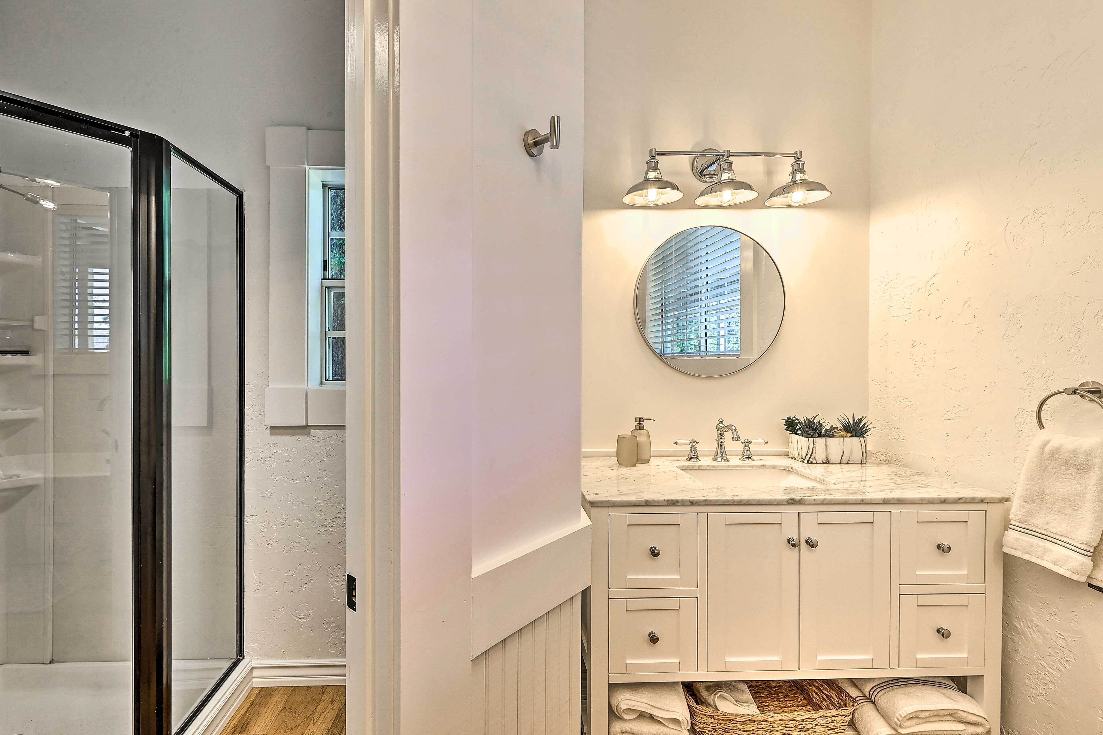 Une salle de bain avec une douche à parois de verre, un miroir rond, un lavabo avec un plan de toilette en marbre et un porte-serviettes.