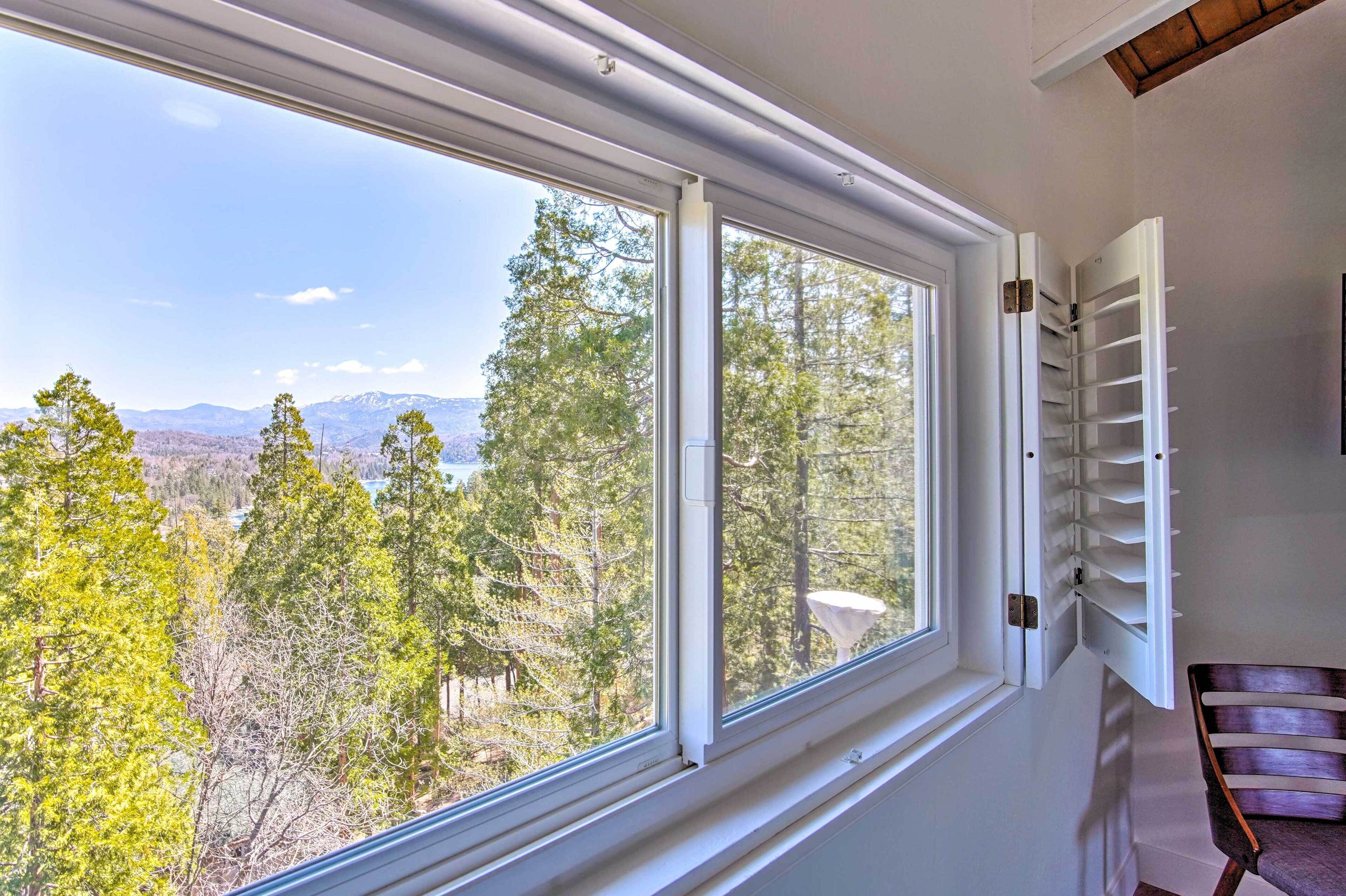 A room with a large window overlooking a forested area and mountains.