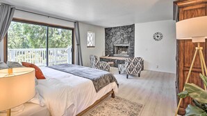 Ein Schlafzimmer mit einem großen Bett, einem Schreibtisch, zwei gemusterten Sesseln, einem Kamin und einem Balkon mit Blick auf Bäume.