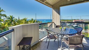 A balcony with a table and chairs, overlooking a coastal view with palm trees and a clear sky. - Top-floor Kailua Bay Resort Condo w/ Ocean Views! (Kailua-Kona)