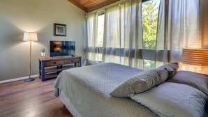 A bedroom with a large bed, a TV on a wooden dresser, and a window with sheer curtains. - Top-floor Kailua Bay Resort Condo w/ Ocean Views! (Kailua-Kona)
