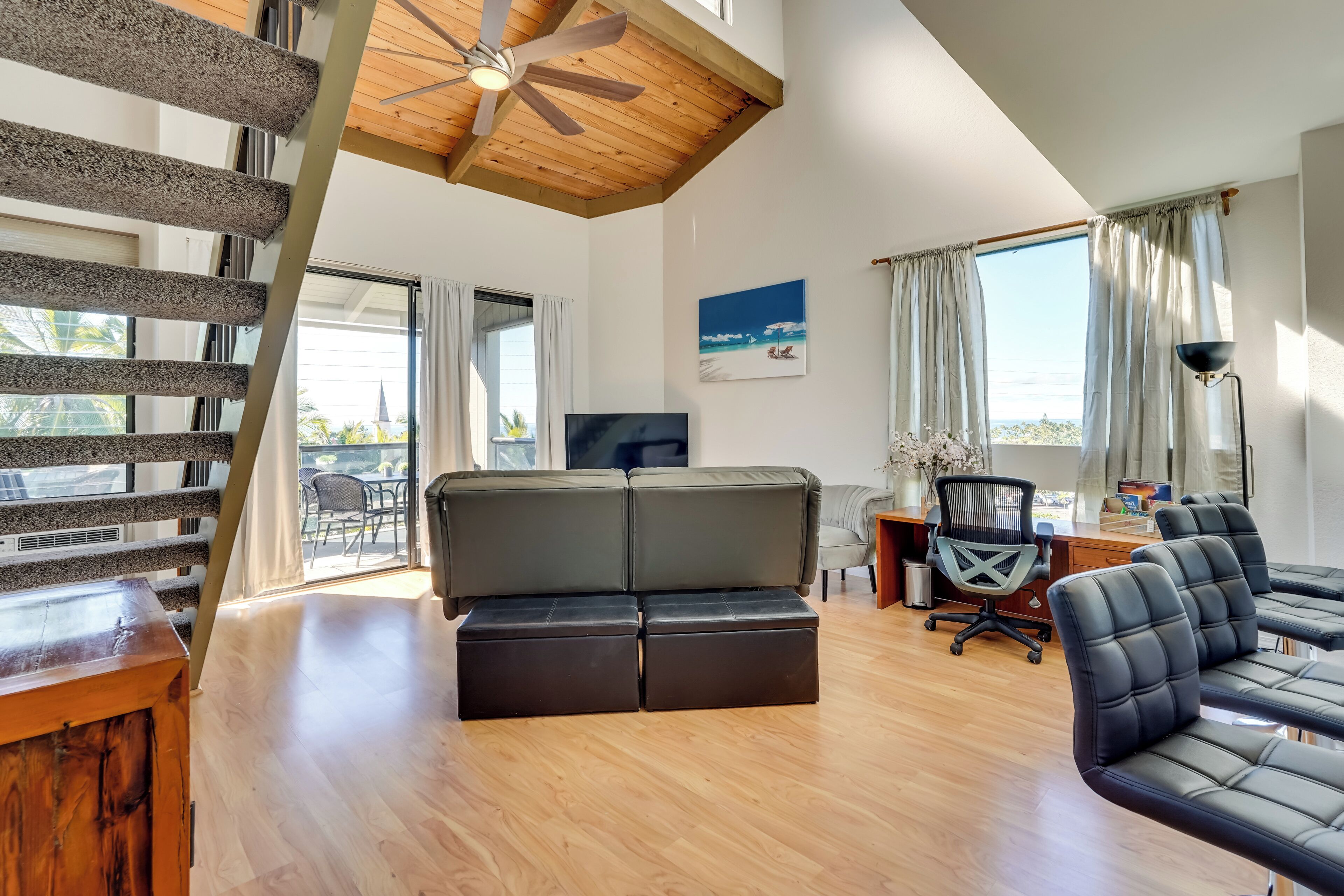 A modern living room with a wooden ceiling, a large window, a green sofa, a desk with a chair, and a TV.