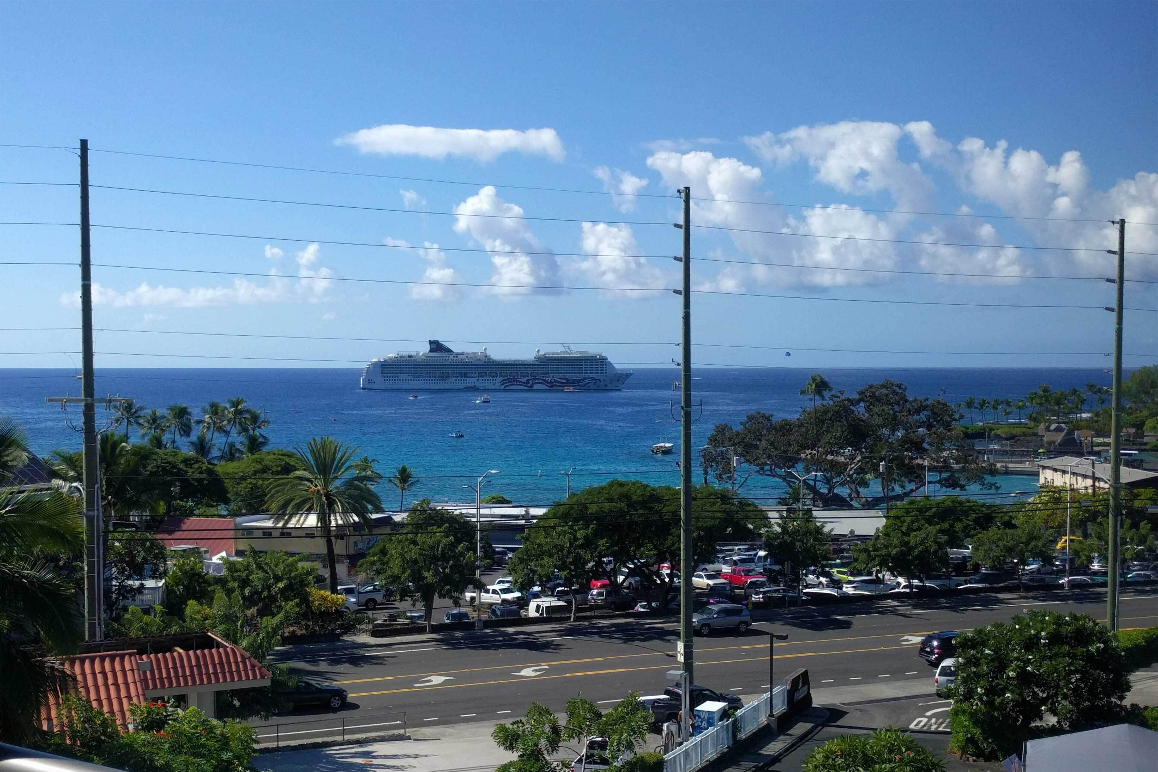A coastal view with a cruise ship in the distance, a parking lot, and a clear blue sky.