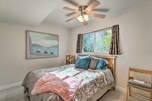 A bedroom with a bed, a ceiling fan, a window with curtains, a chair, and a framed picture on the wall.