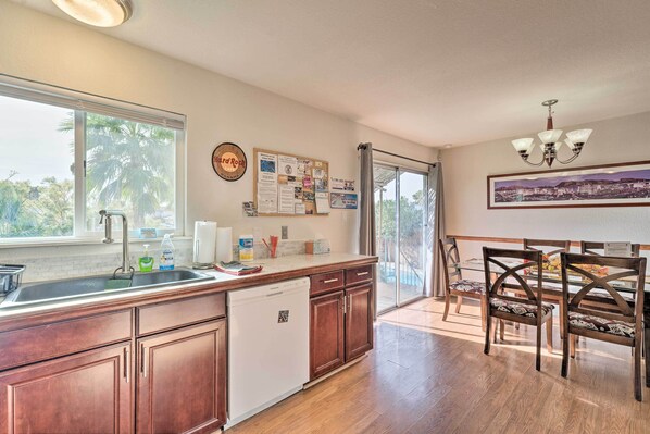 A kitchen with wooden cabinets, a dishwasher, a large window, and a dining area with a table and chairs. - 'vegas Oasis' Home w/ Pool & Spa: 7 Miles to Strip (Las Vegas)