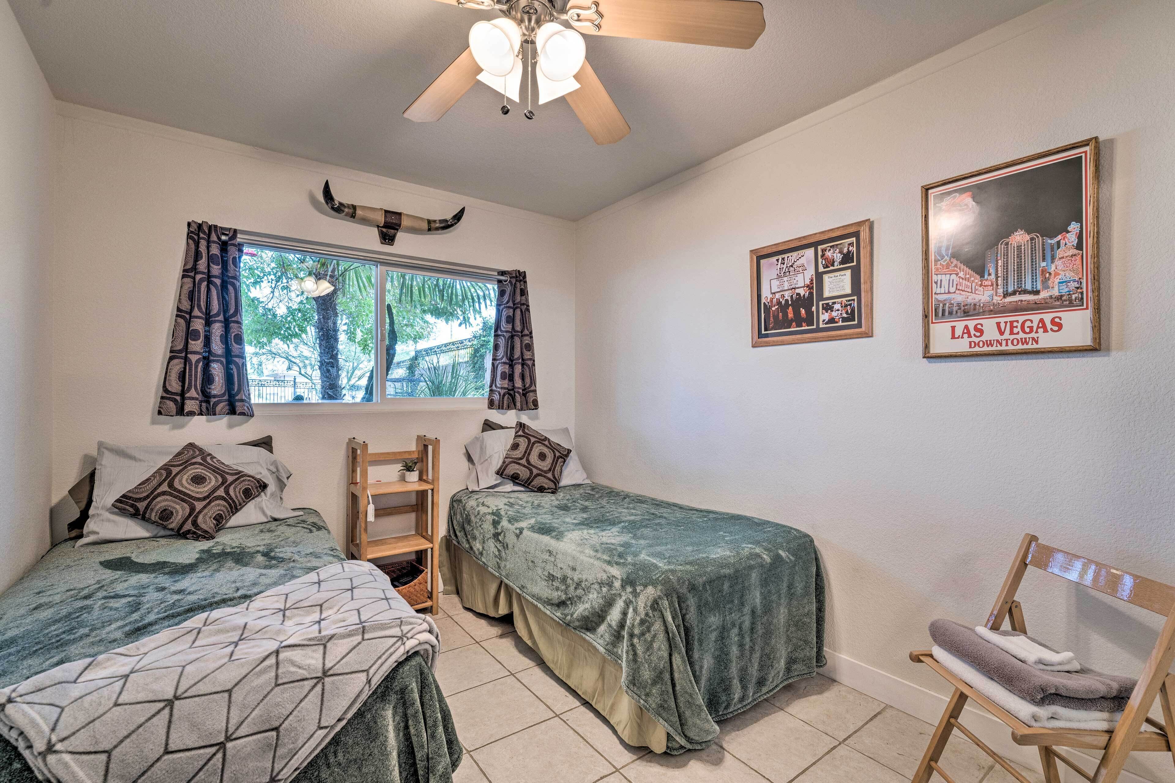 A bedroom with two beds, a ceiling fan, a window with curtains, and two framed pictures on the wall.
