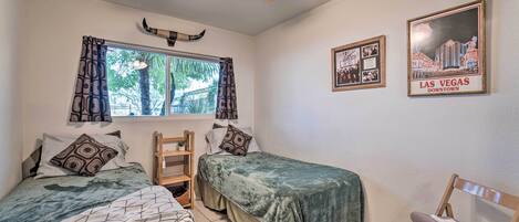 A bedroom with two beds, a ceiling fan, a window with curtains, and two framed pictures on the wall.