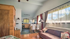 Ein gemütliches Zimmer mit einem Holzschrank, einer Couch mit floralen Kissen, einem Essbereich mit Tisch und Stühlen sowie einer Küche im Hintergrund.