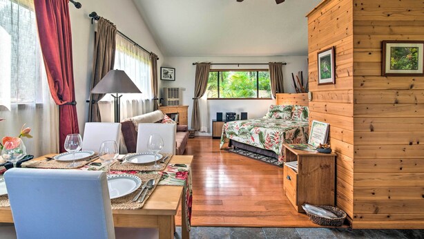 Ein gemütliches Zimmer mit Deckenventilator aus Holz, einem Bett mit blumigem Überwurf, einem Esstisch für zwei Personen und einem Fenster mit Vorhängen.