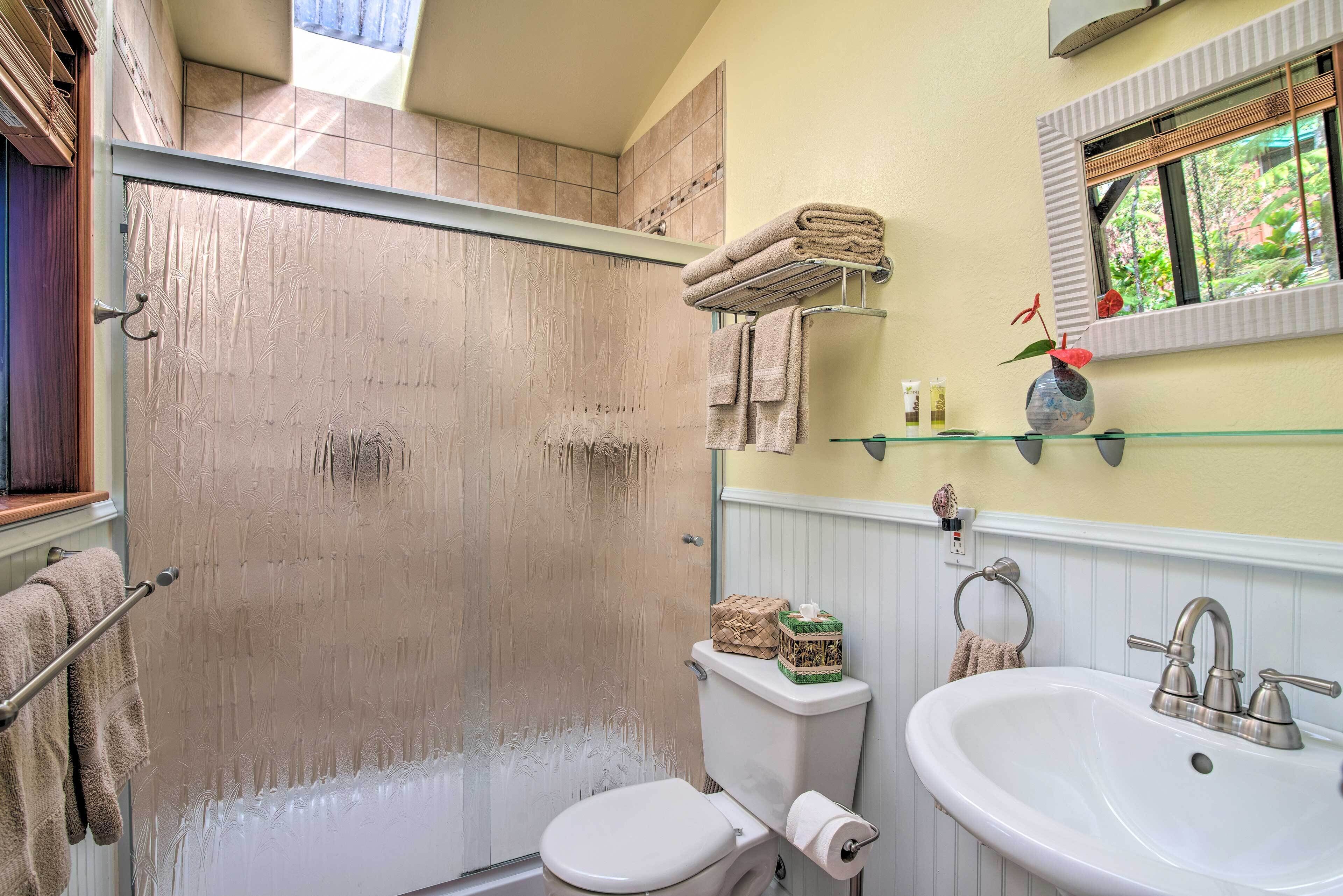 Une salle de bain équipée d’une douche, de toilettes, d’un lavabo et d’une fenêtre donnant sur un espace verdoyant.