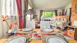 Ein gut beleuchteter Raum mit einem Esstisch für zwei Personen, einem Bett mit Blumenmuster und einer hölzernen Kommode.