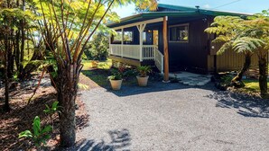 Ein Haus mit Veranda, umgeben von Grünpflanzen und einer Schotterauffahrt.