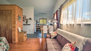 Ein gemütliches Wohnzimmer mit einem Holzschrank, einer Couch mit floralen Kissen und einem Essbereich im Hintergrund.