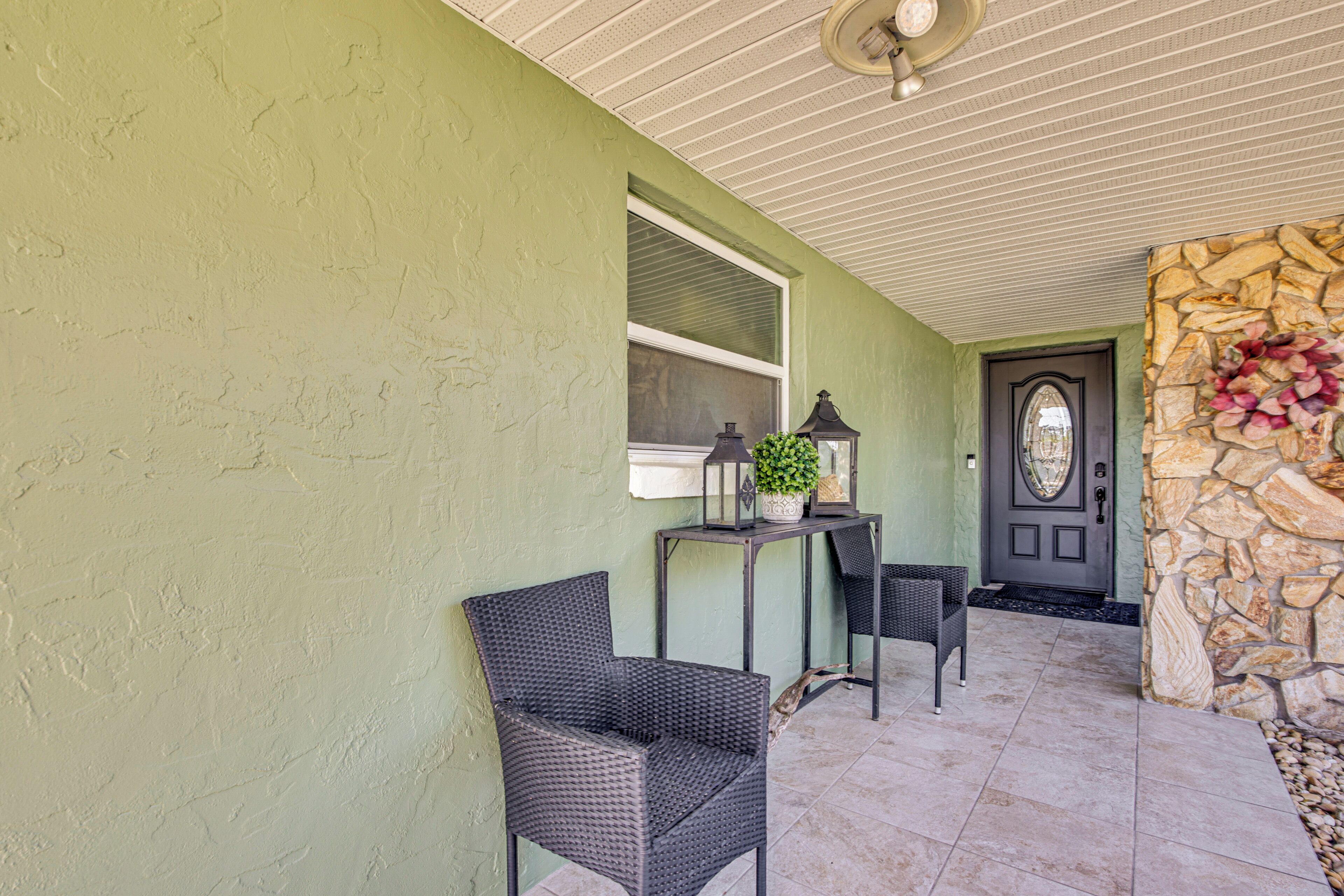 A covered porch with wicker chairs, a small table with a plant, and a stone wall.