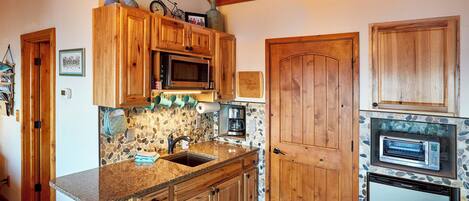A kitchen with wooden cabinets, a built-in microwave, a toaster oven, and a stone backsplash.