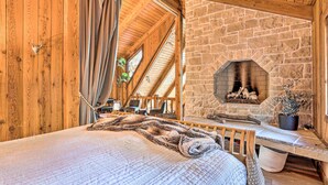 A cozy room with a stone fireplace, wooden ceiling beams, and a bed with a patterned blanket. - Cimarron Lodge Retreat With 3 Decks & Grill! (Cedar Glen)