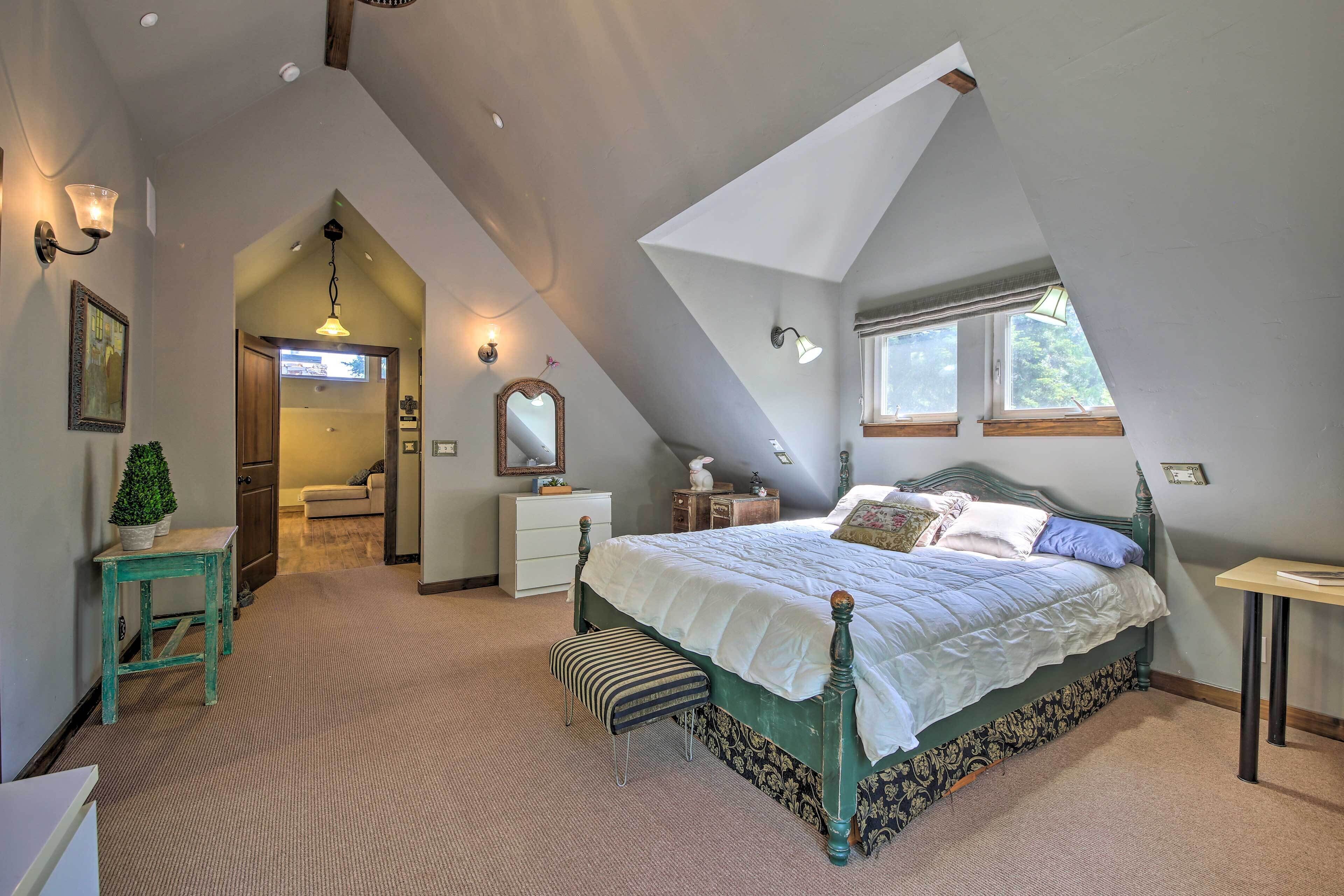 A bedroom with a large bed, a small table, a bench, and a window.