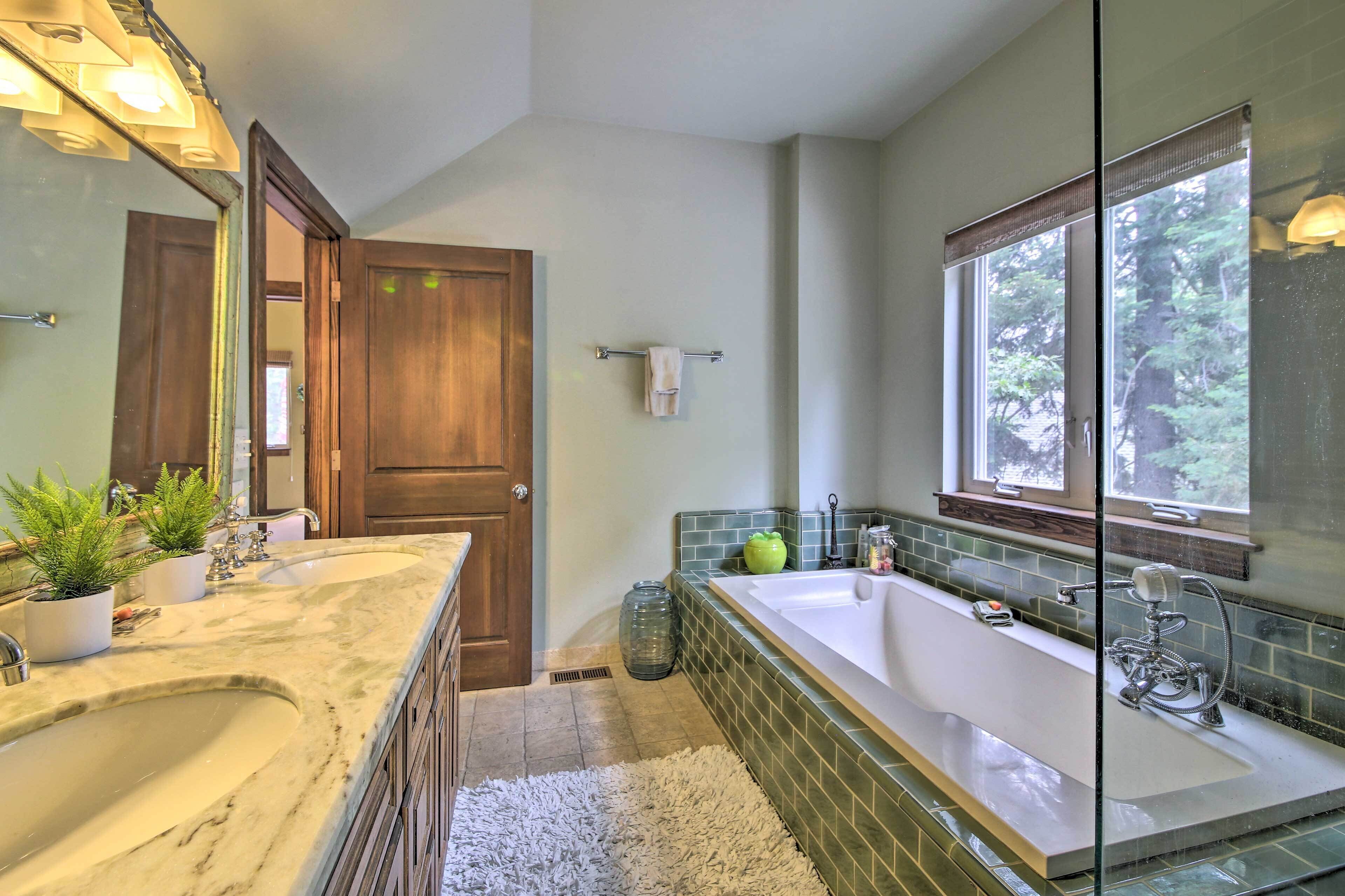 Ein Badezimmer mit einer großen Badewanne, einem Doppelwaschbecken, einem Spiegel und einem Fenster mit Blick auf Bäume.
