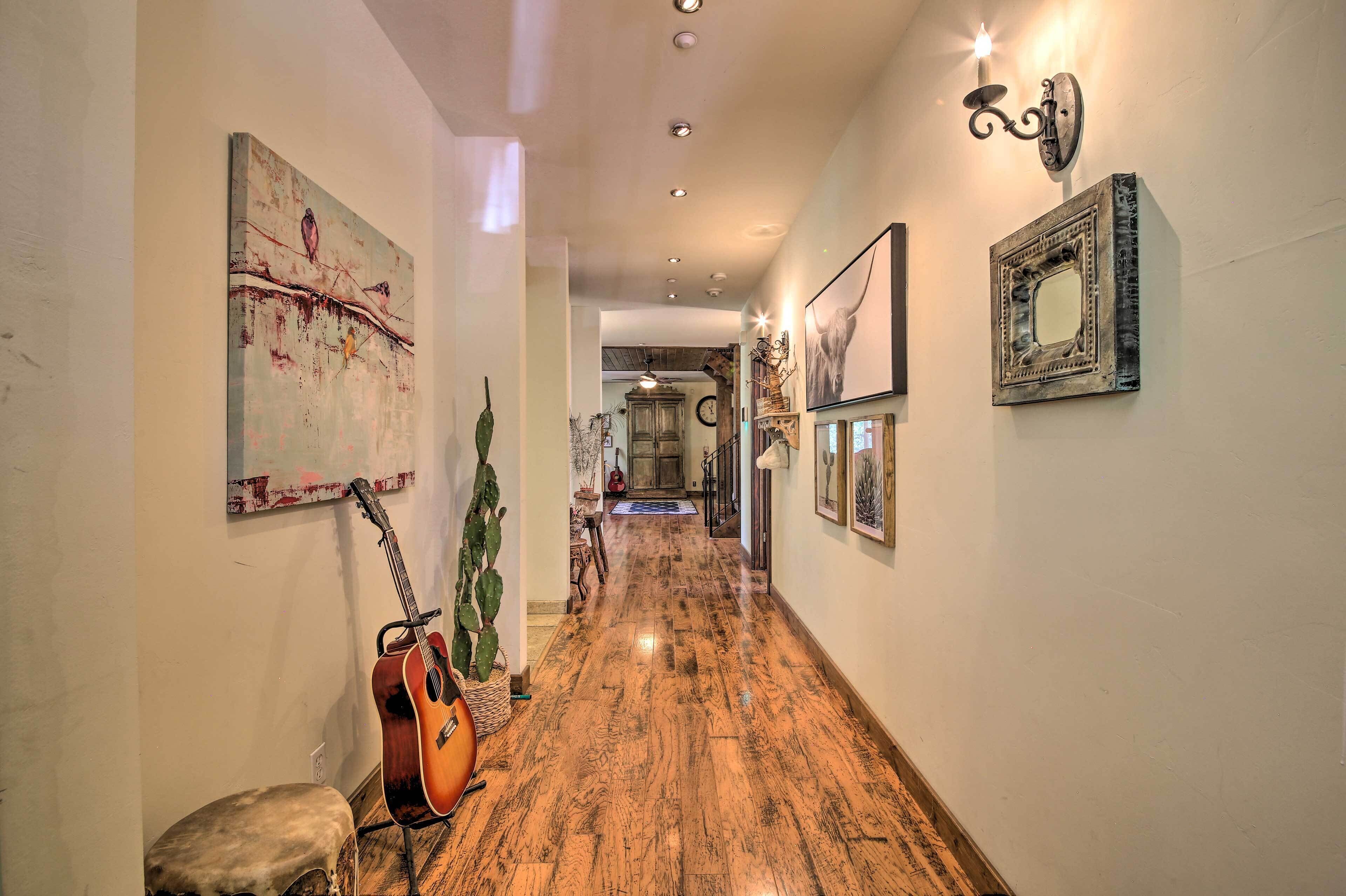 A hallway with wooden flooring, a guitar leaning against a wall, and various framed pictures and artwork.