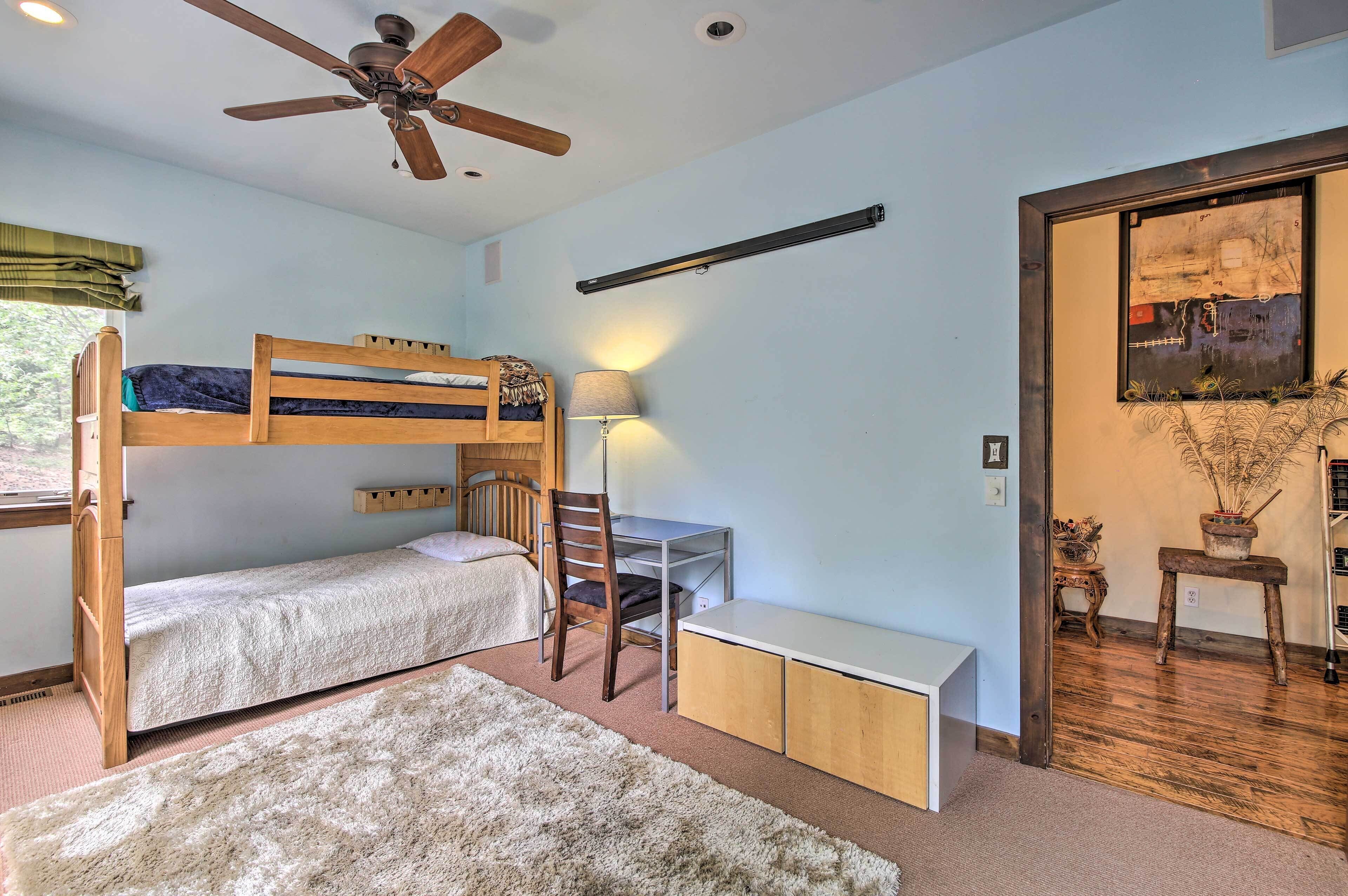 A room with bunk beds, a desk, a chair, a lamp, and a ceiling fan.