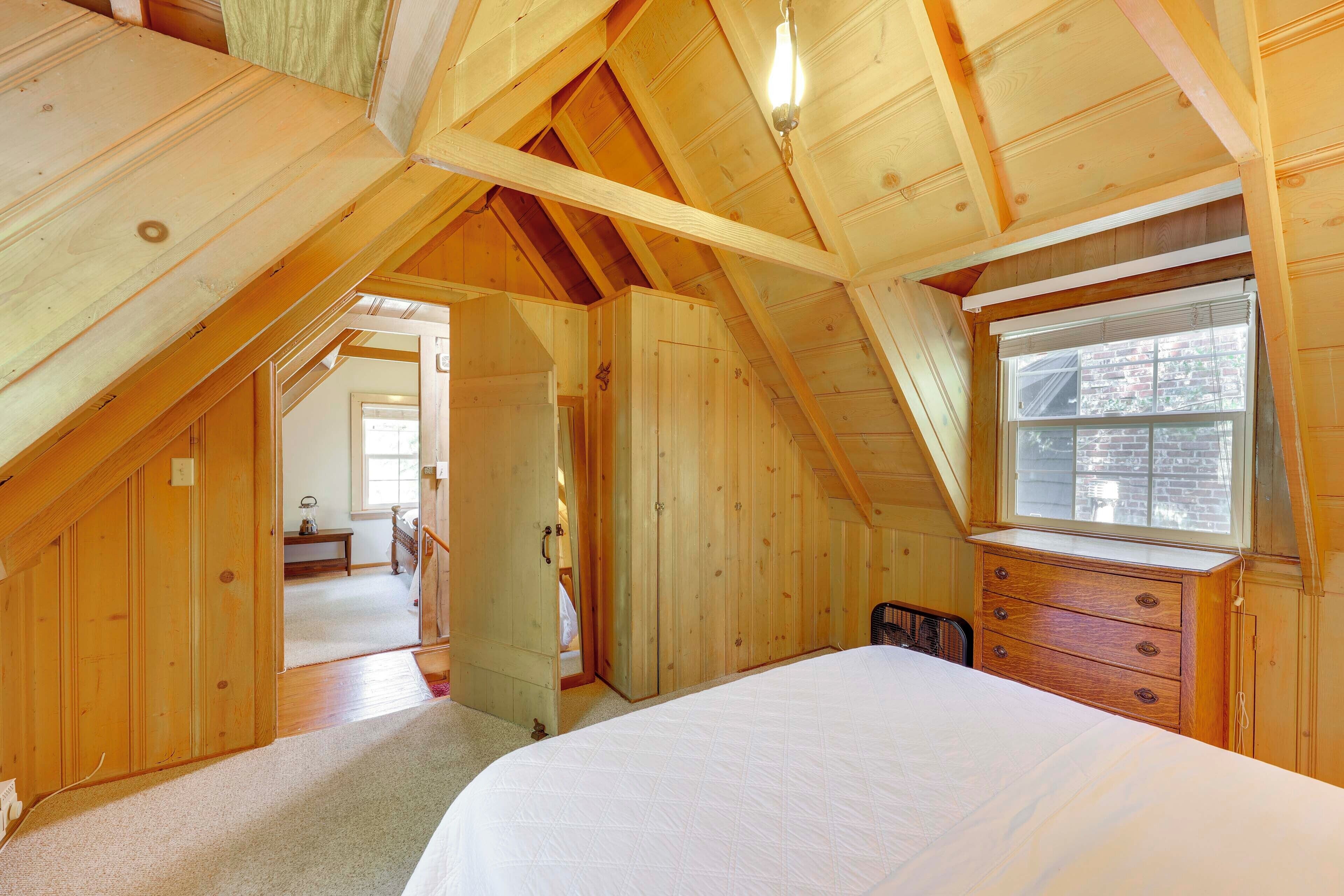 Une chambre avec un plafond en pente, des murs en bois, un lit, une commode et une fenêtre.