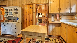 Un interior de madera con una mesa de comedor, un aparador blanco con puertas de cristal y una zona de cocina con armarios de madera y encimera.