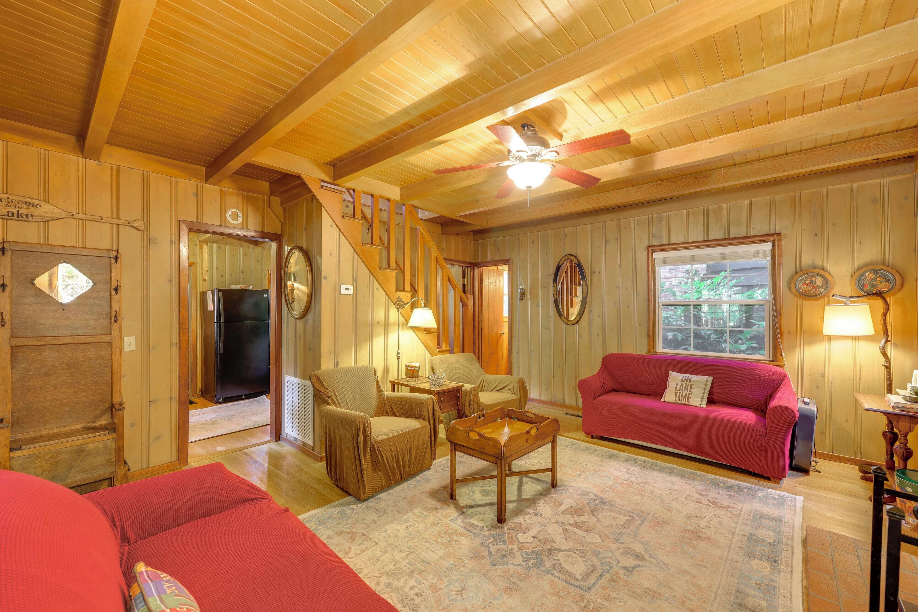 A cozy cabin interior with a wooden ceiling, a red couch, a wooden coffee table, and a staircase leading to another room.