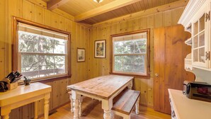 Un interior de madera con una mesa, un banco y una ventana con vistas a árboles.
