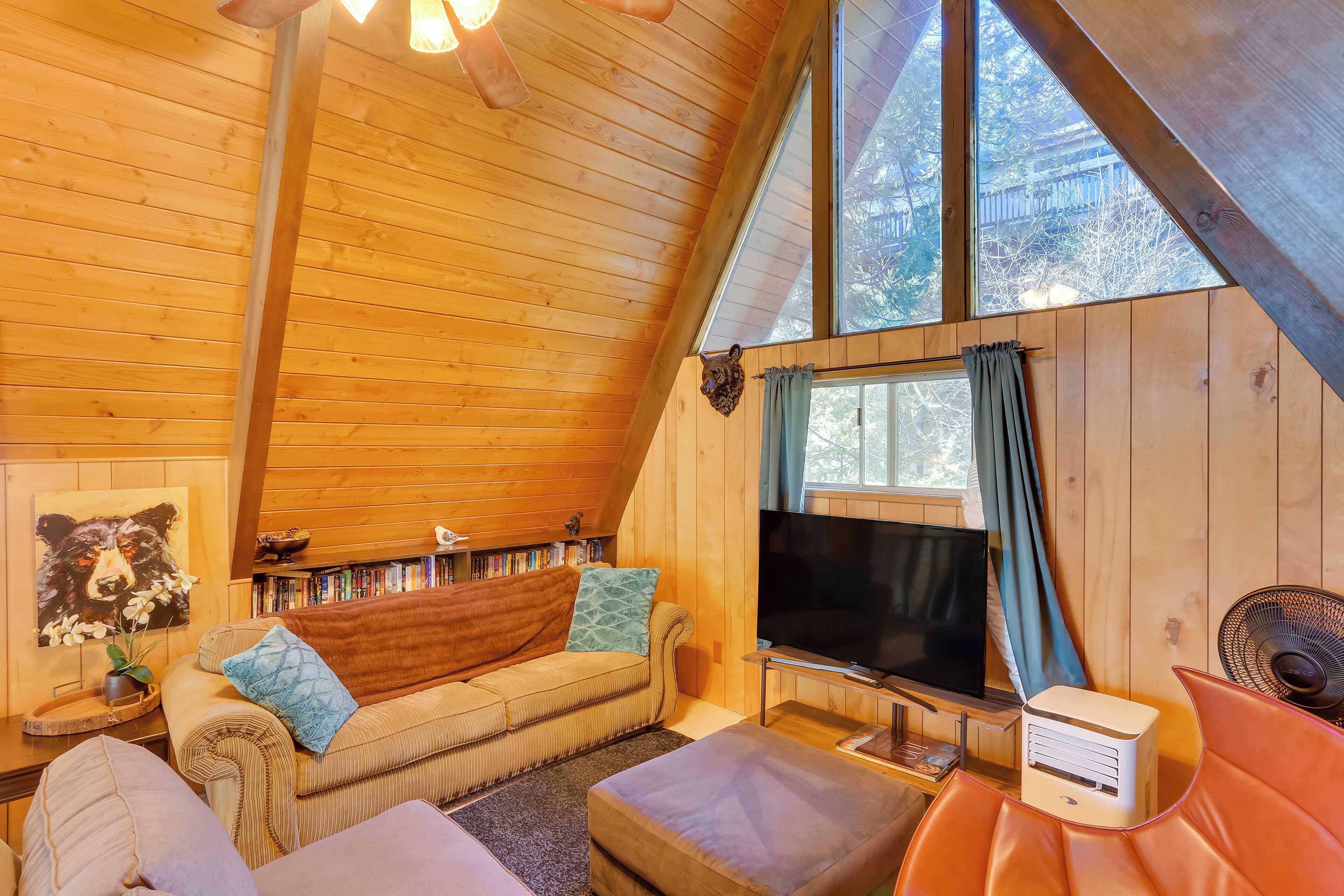 Ein gemütliches Blockhaus-Interieur mit Holzbalkendecke, einer Couch, einem Fernseher und einem Ventilator.
