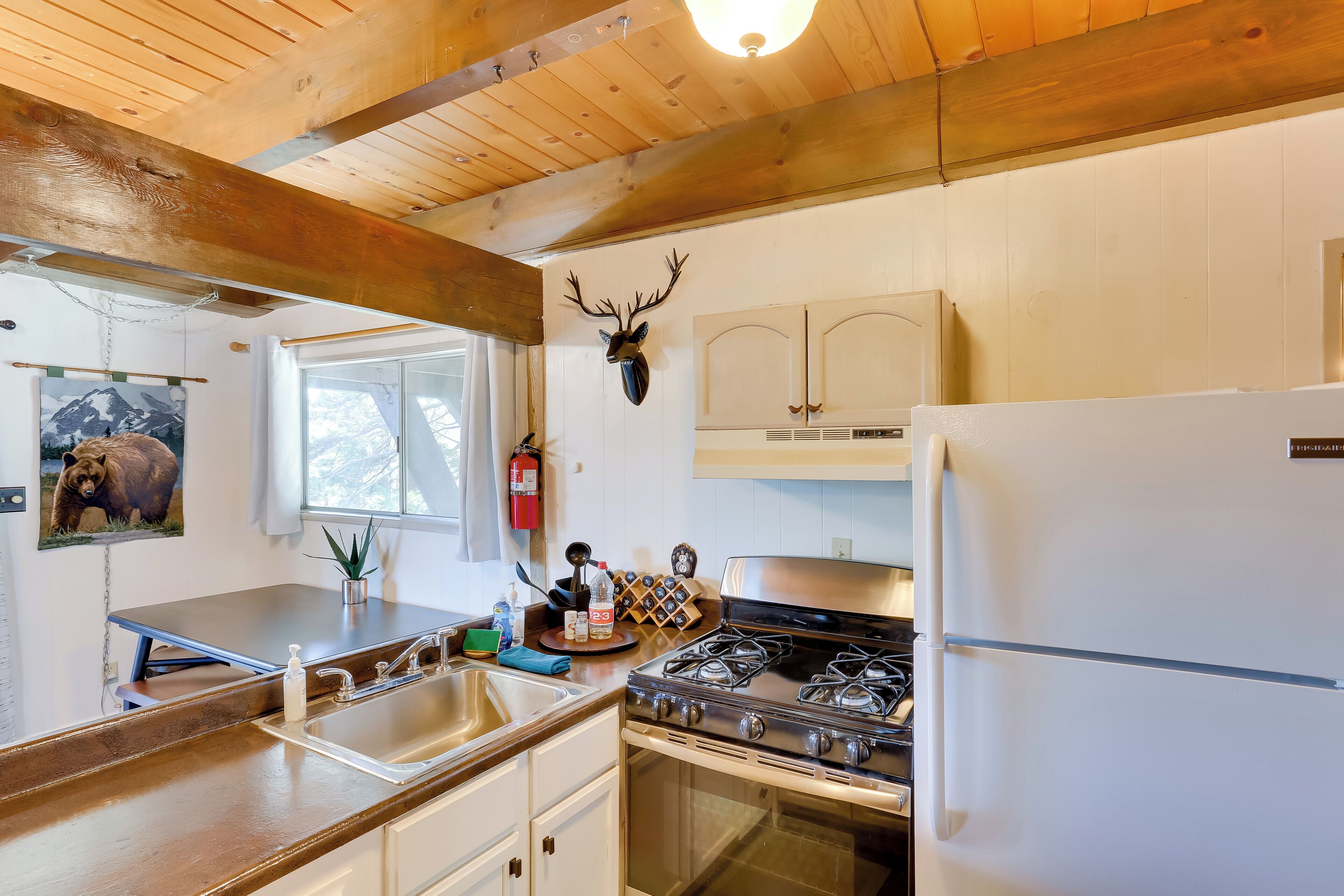 A kitchen with wooden beams, a gas stove, a sink, and a mounted deer head.