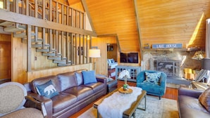 A cozy cabin interior with a wooden staircase, leather sofas, a stone fireplace, and a sign reading "LAKE HOUSE". - A-frame Home w/ 3 Decks & Lake Arrowhead Views! (Lake Arrowhead)