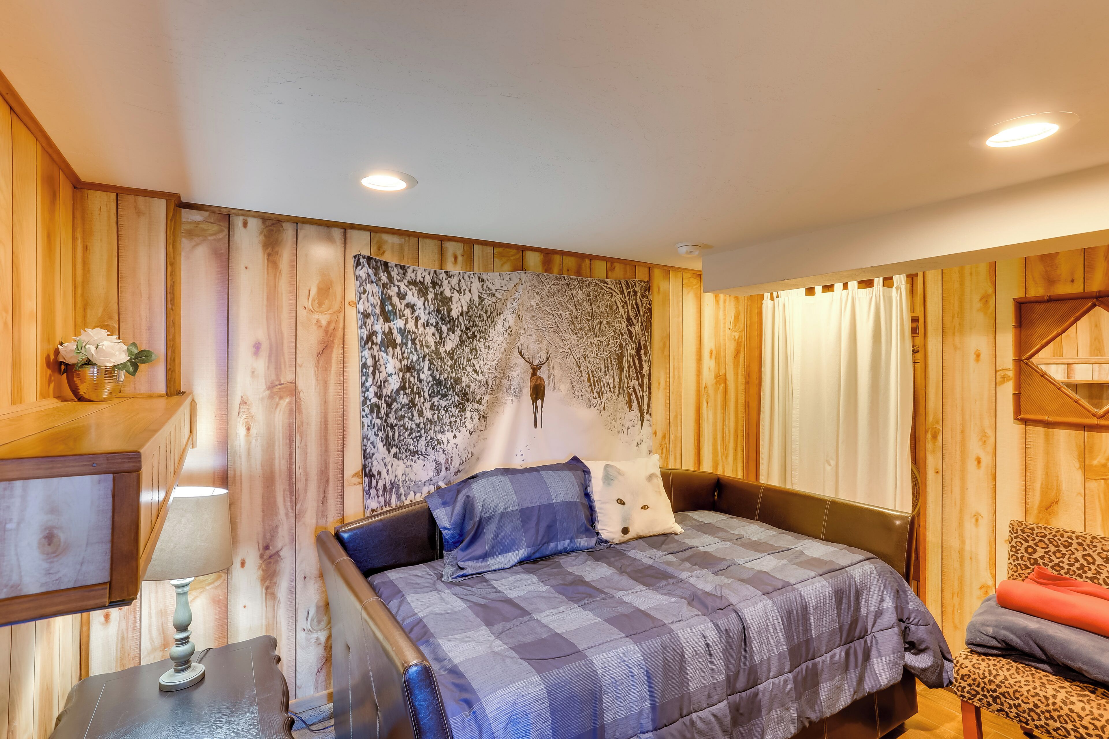 A wooden-paneled room with a bed, a nightstand, a lamp, and a wall tapestry.