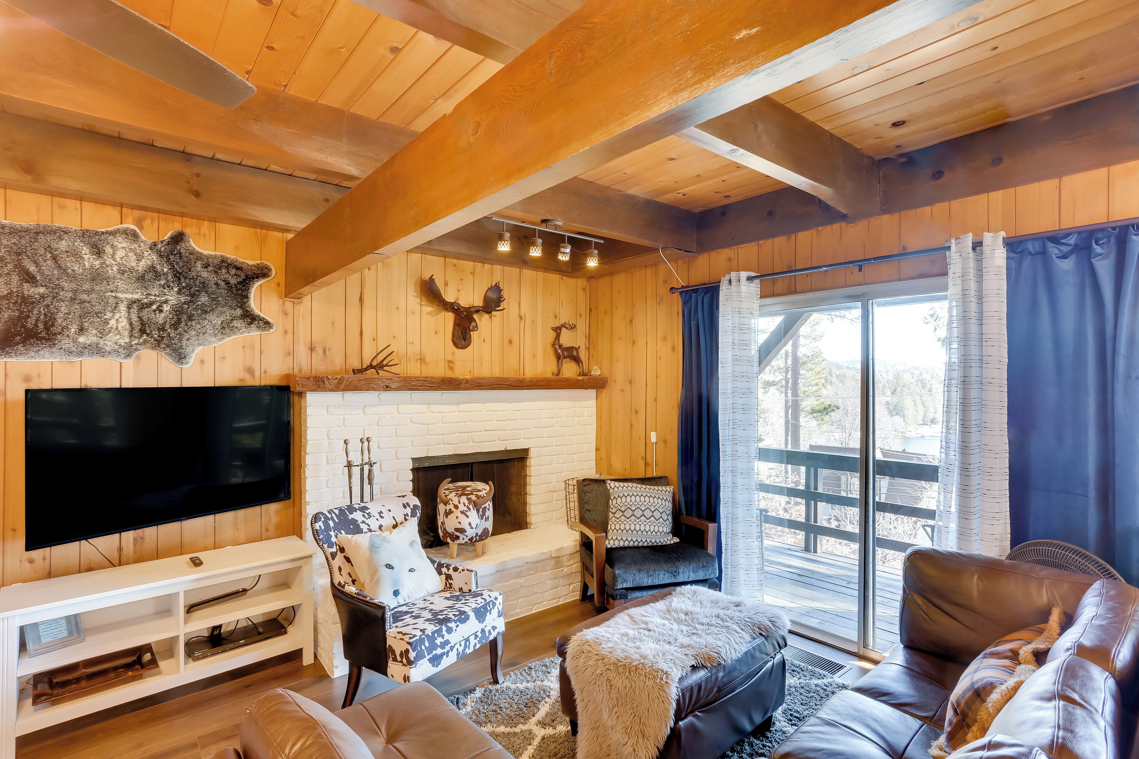 A cozy cabin interior with a fireplace, wooden walls, a television, and a large window.